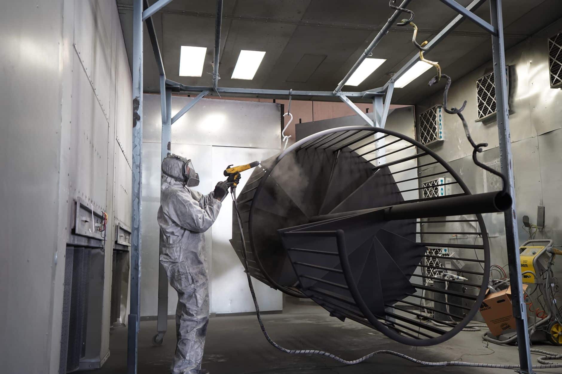 Technician spraying a metal part in an industrial booth where vapour and static charge matter